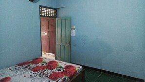 Une pièce avec un lit, une porte et un ventilateur fixé au mur.