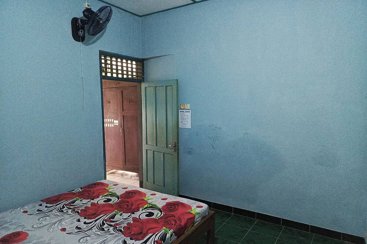Ein Zimmer mit einem Bett, einer Tür und einem Wandventilator.