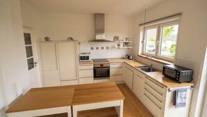 Una cucina compatta con mobili bianchi, un tavolo di legno, un forno a microonde, un forno e una finestra con vista all'esterno.