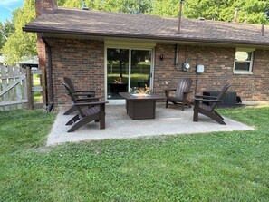 Une maison en briques avec un patio, deux fauteuils Adirondack, un foyer extérieur et une porte-fenêtre coulissante.