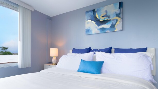 Une chambre à coucher avec un lit, une table de chevet, une lampe et une fenêtre avec des rideaux.