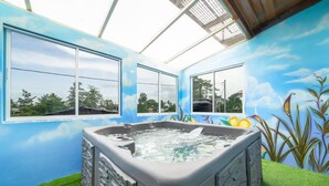 Un bain à remous avec un revêtement extérieur en pierre, de grandes fenêtres et une fresque représentant un ciel et des plantes.