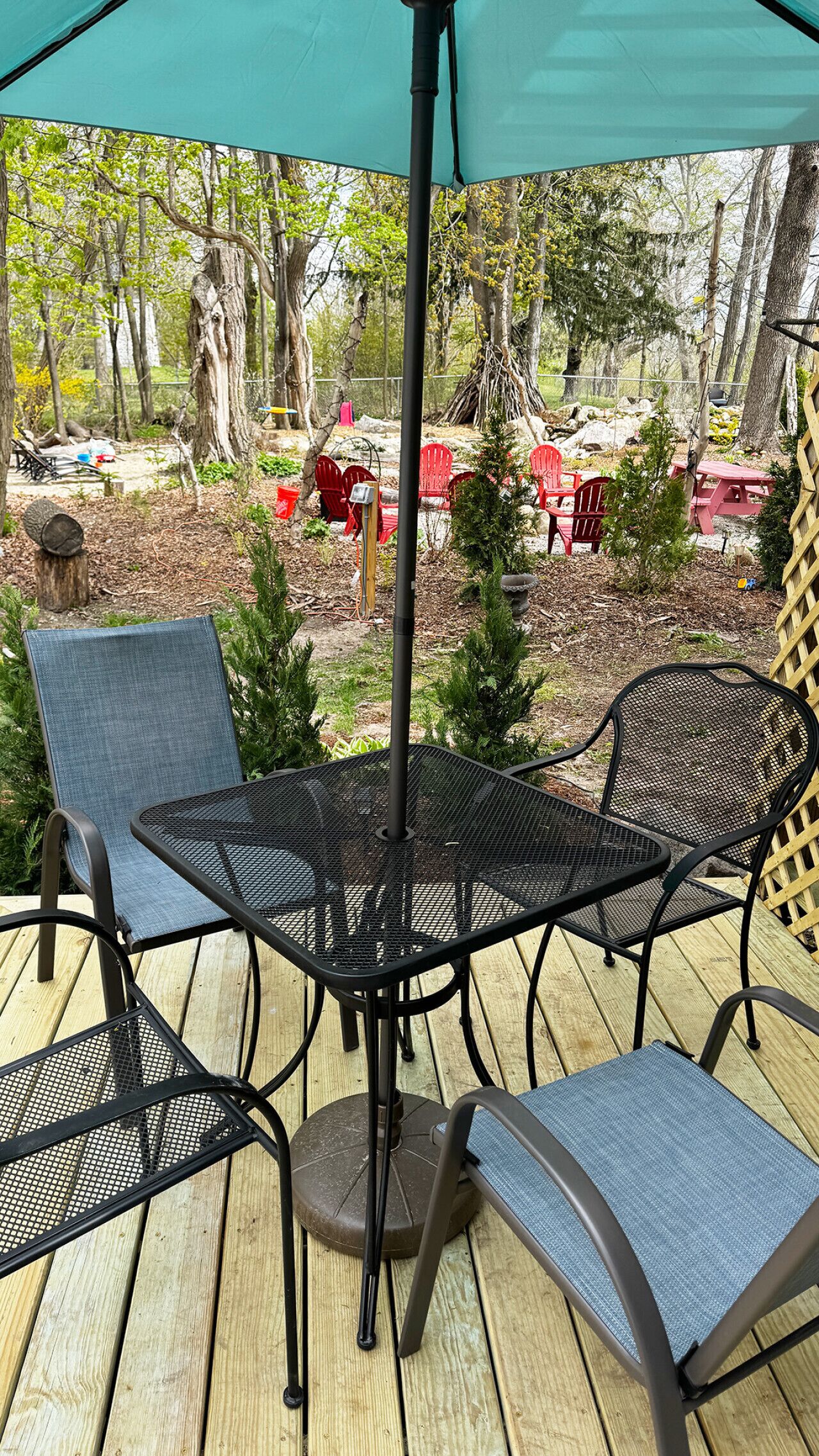 A wooden deck with a metal table and chairs, surrounded by trees and outdoor furniture.