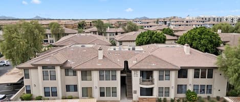 A multi-story residential building with a flat roof, multiple balconies, and a parking lot with several cars.