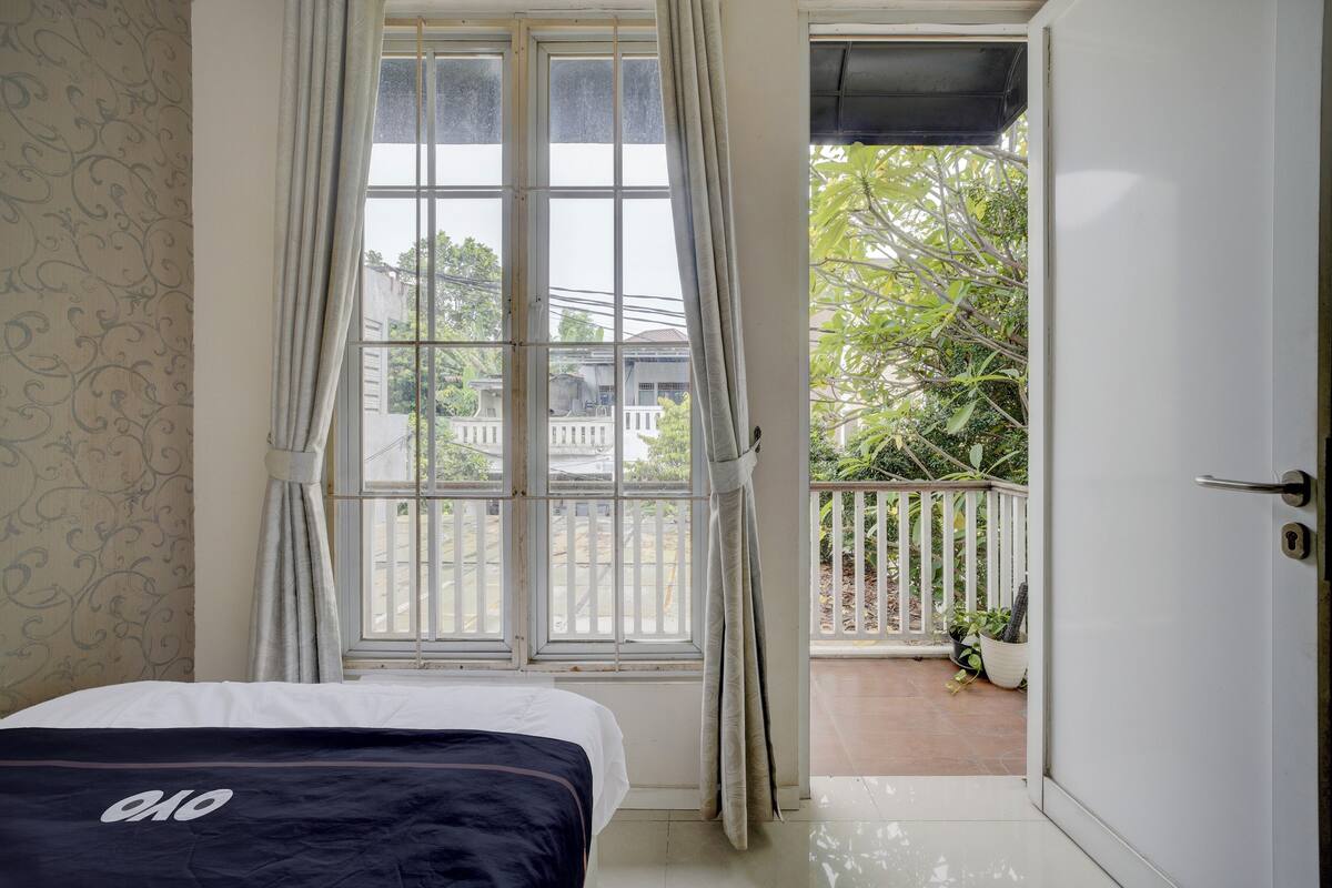 A bedroom with a bed, a window with curtains, a balcony with a railing, and a door.