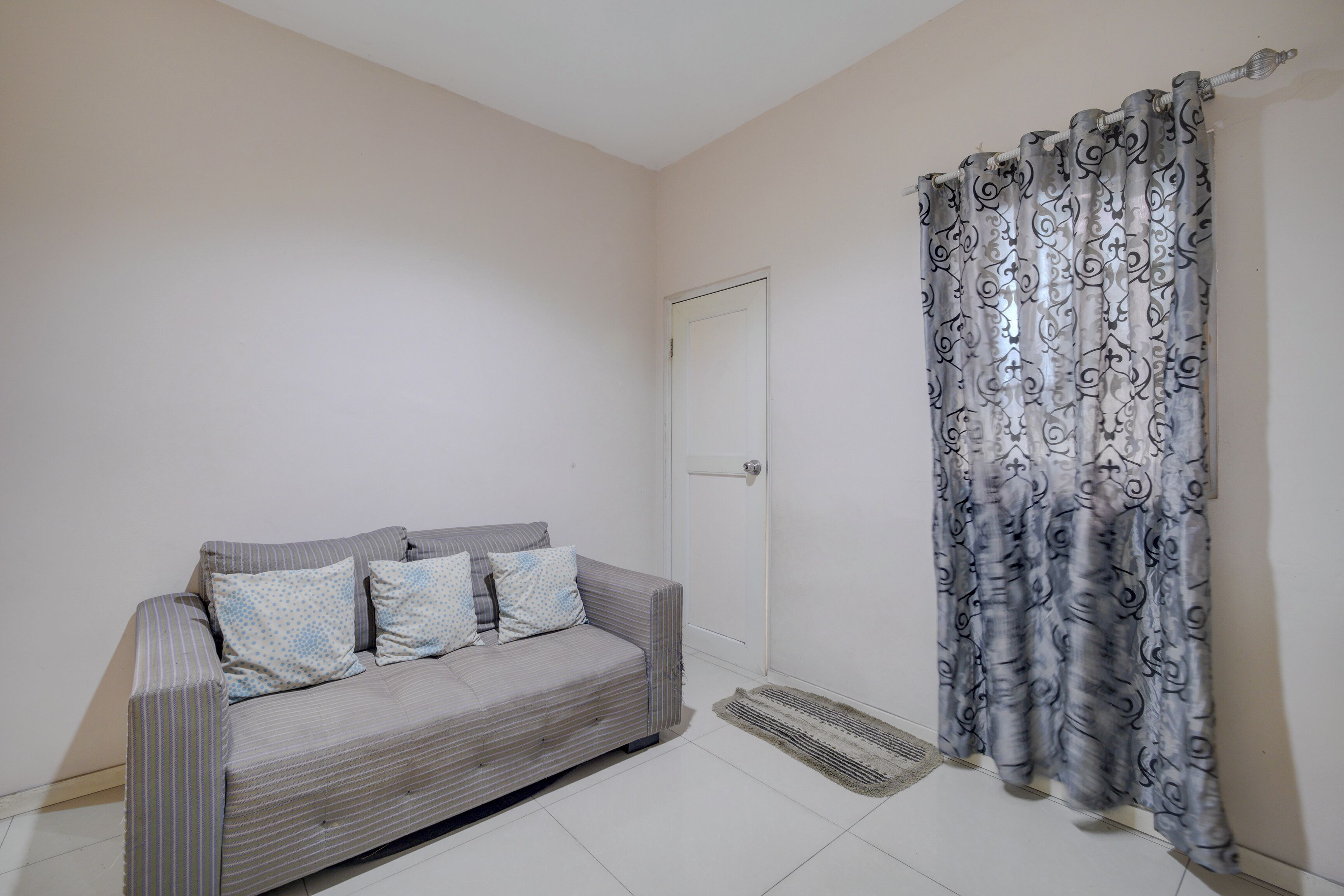 A room with a striped sofa, patterned curtains, a door, and a tiled floor.