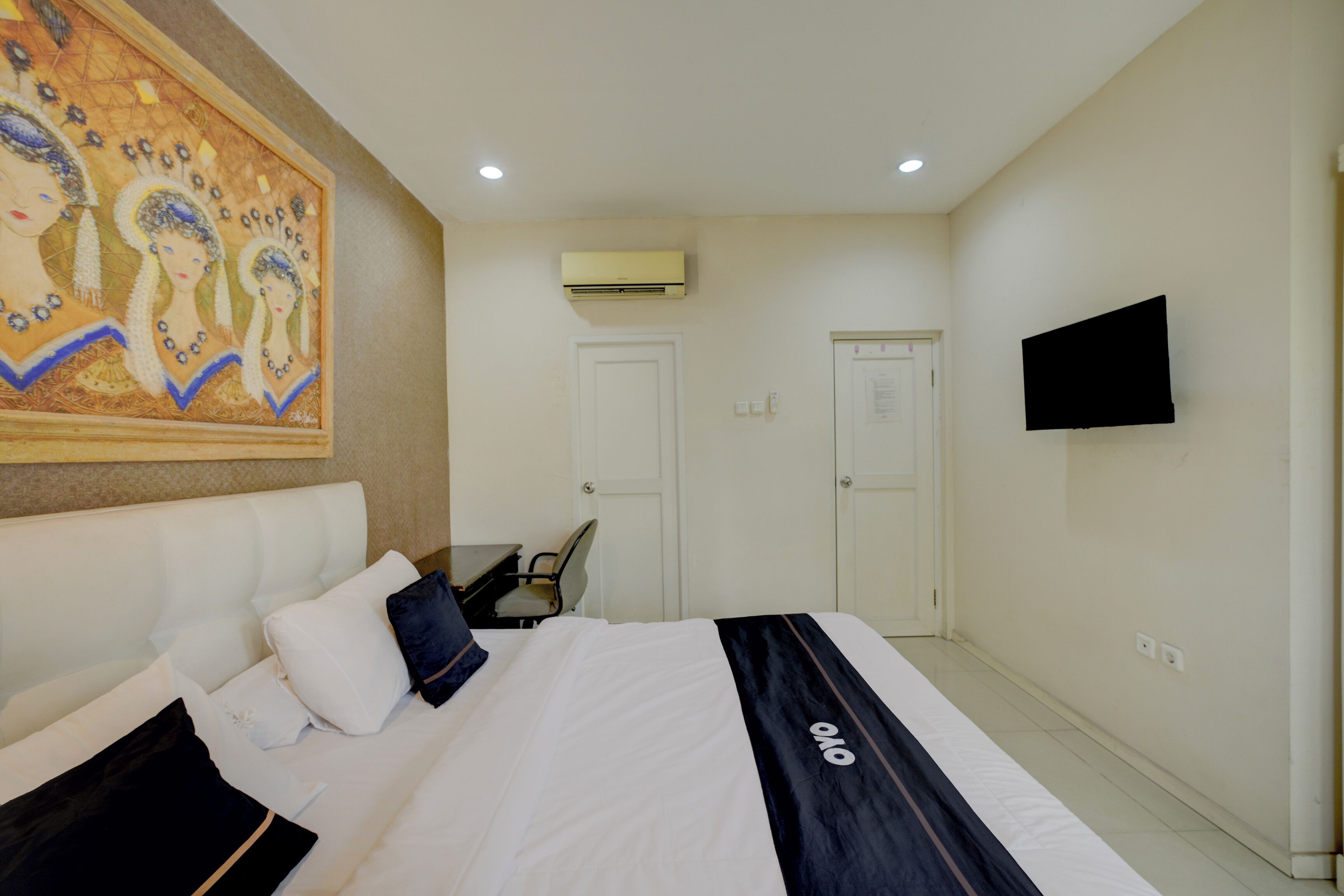 Habitación de hotel con cama, escritorio, silla, televisor de pantalla plana, aire acondicionado y puerta.