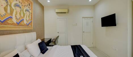 Habitación de hotel con cama, escritorio, silla, televisor de pantalla plana, aire acondicionado y puerta.