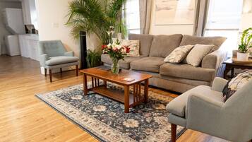 A living room with a sofa, two armchairs, a coffee table, a patterned rug, and a large potted plant.