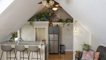 A compact kitchen with a central island, bar stools, a ceiling fan, and a refrigerator.