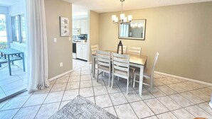 A dining area with a table and chairs, a kitchen in the background, and a view through a glass door. - The Seaside Sanctuary - Walk To The Beach and Pool (Jupiter)
