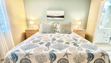 Une chambre à coucher avec un lit agrémenté d’une couvre-lit sur le thème de la mer, deux lampes de chevet, une table de chevet et un tableau accroché au mur.