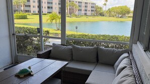 A sunroom with a view of a golf course, a wooden table, and a sectional sofa. - The Seaside Sanctuary - Walk To The Beach and Pool (Jupiter)