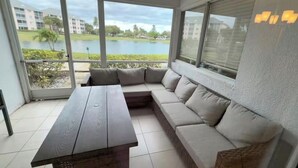 A modern room with a large window, a sectional sofa, and a wooden table. - The Seaside Sanctuary - Walk To The Beach and Pool (Jupiter)