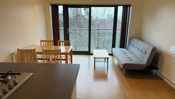 A modern kitchen with a dining table and chairs, a sofa, and a large window with a view of trees.