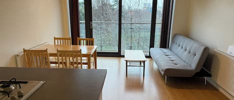 A modern kitchen with a dining table and chairs, a sofa, and a large window with a view of trees.