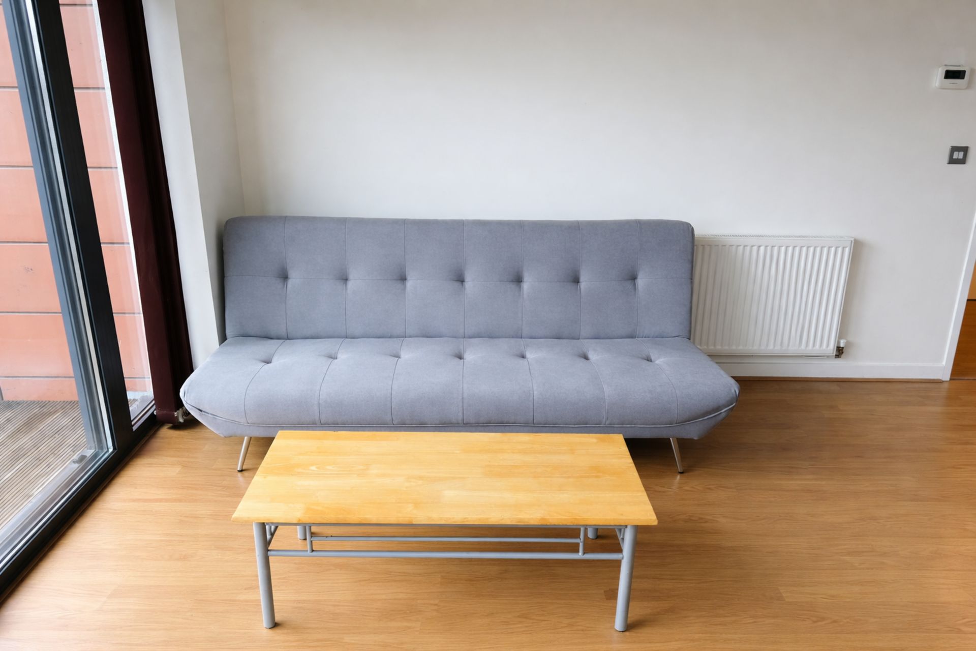 A grey sofa and a wooden table in a room with wooden flooring and a white radiator.