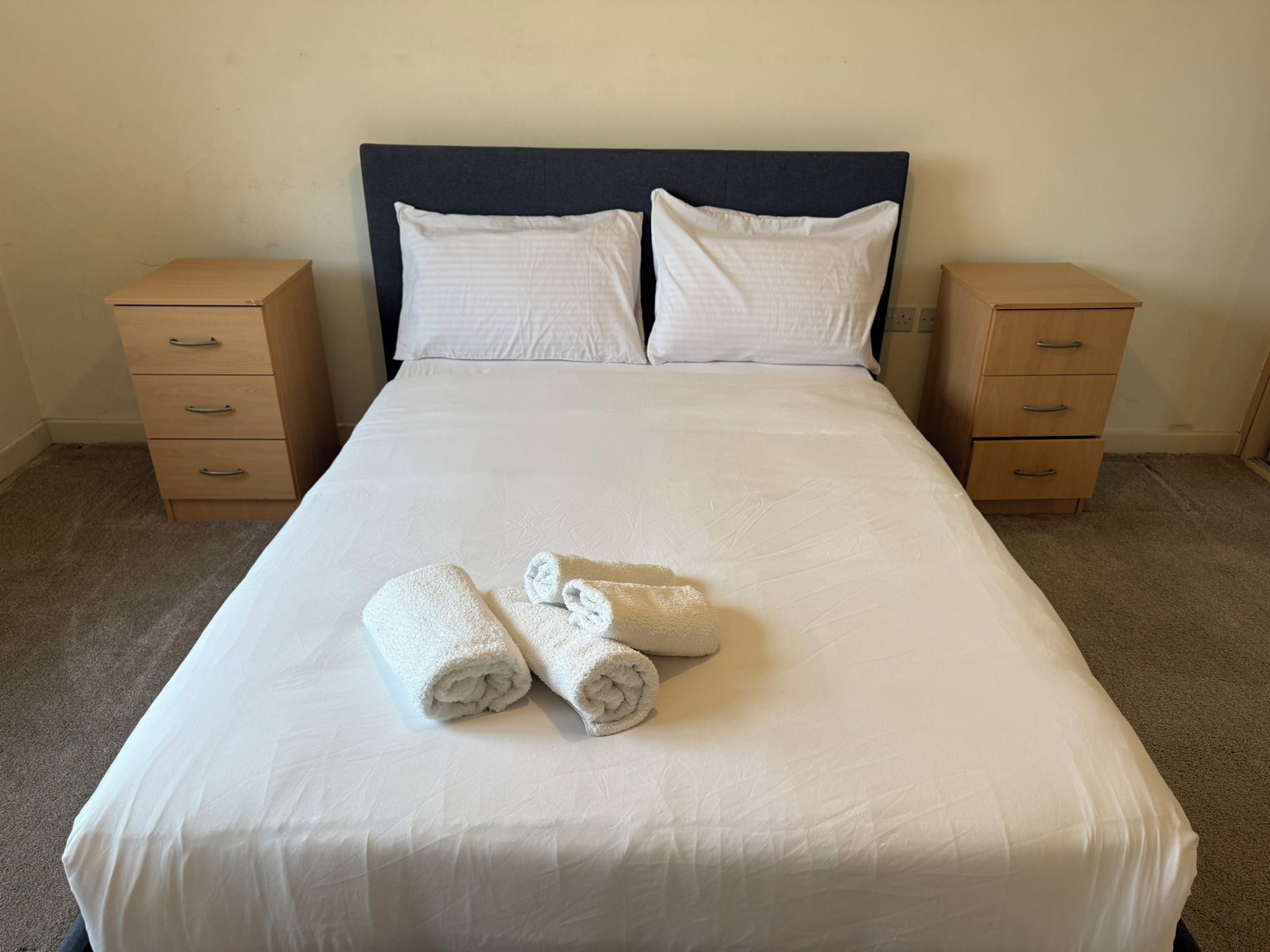 A neatly made bed with white linens and two rolled towels placed on the bed.