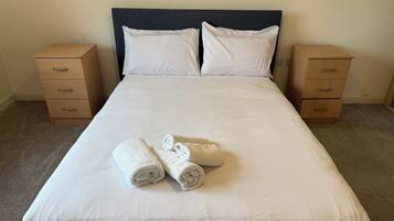 A neatly made bed with white linens and two rolled towels placed on the bed.
