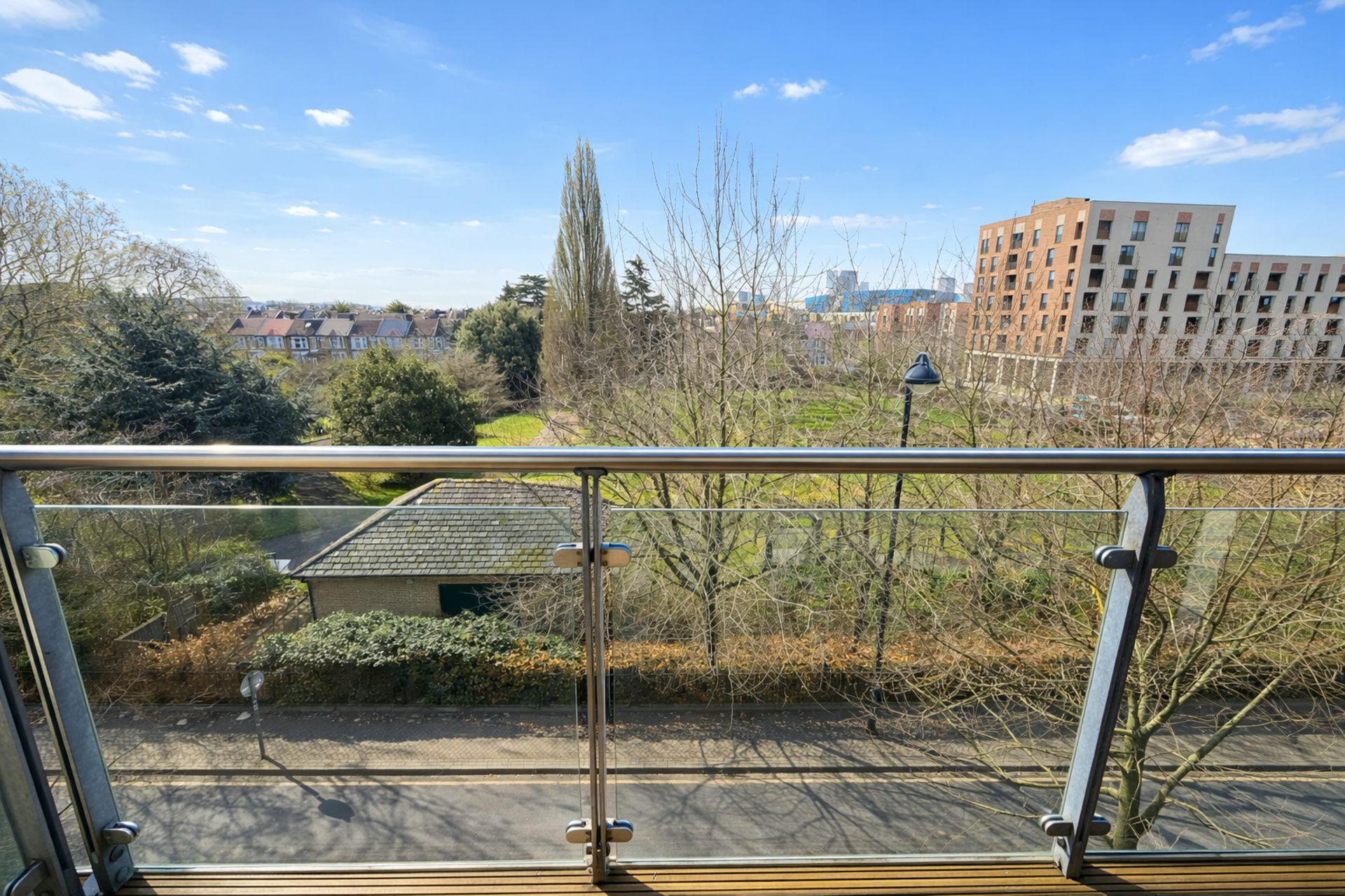 Vista da un balcone con ringhiera in metallo, su un parco con alberi e un edificio sullo sfondo.