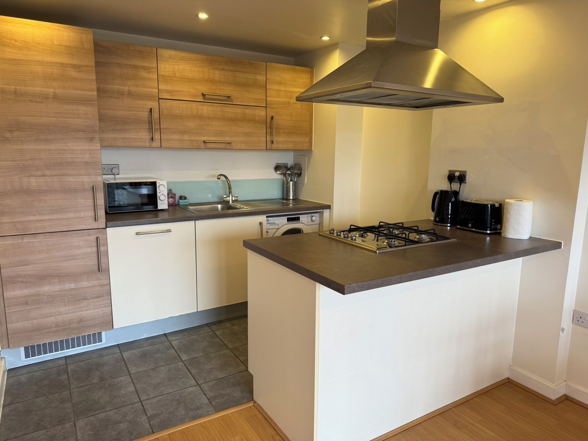 A modern kitchen with a central island, built-in microwave, stainless steel sink, and a range hood.