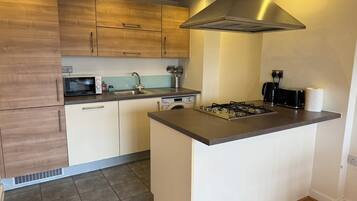 A modern kitchen with a central island, built-in microwave, stainless steel sink, and a range hood.