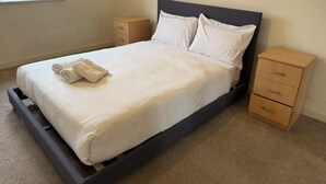 Een enkel bed met een houten frame en een donker hoofdbord, met twee nachtkastjes en een raam met gordijnen.