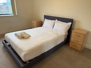 A single bed with a wooden frame and a dark headboard, accompanied by two bedside tables and a window with curtains. - Bright 1BDR Apartment with Park Views in Leyton (Greater London)