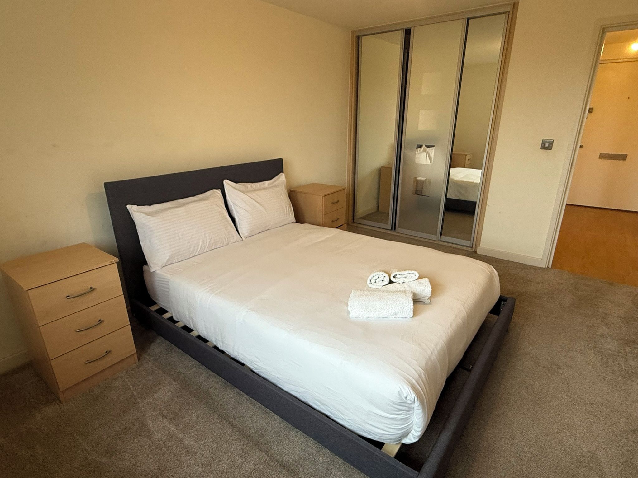 A single bed with a wooden frame, a bedside table, a mirror, and a wardrobe.