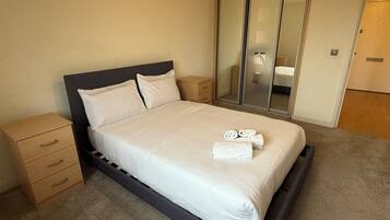 A single bed with a wooden frame, a bedside table, a mirror, and a wardrobe.