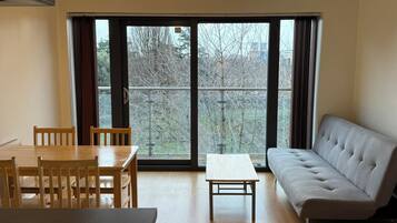 A room with a dining table, chairs, a sofa, and a view through large windows.