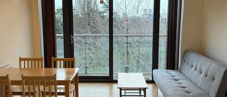 Et værelse med spisebord, stole, sofa og udsigt gennem store vinduer.