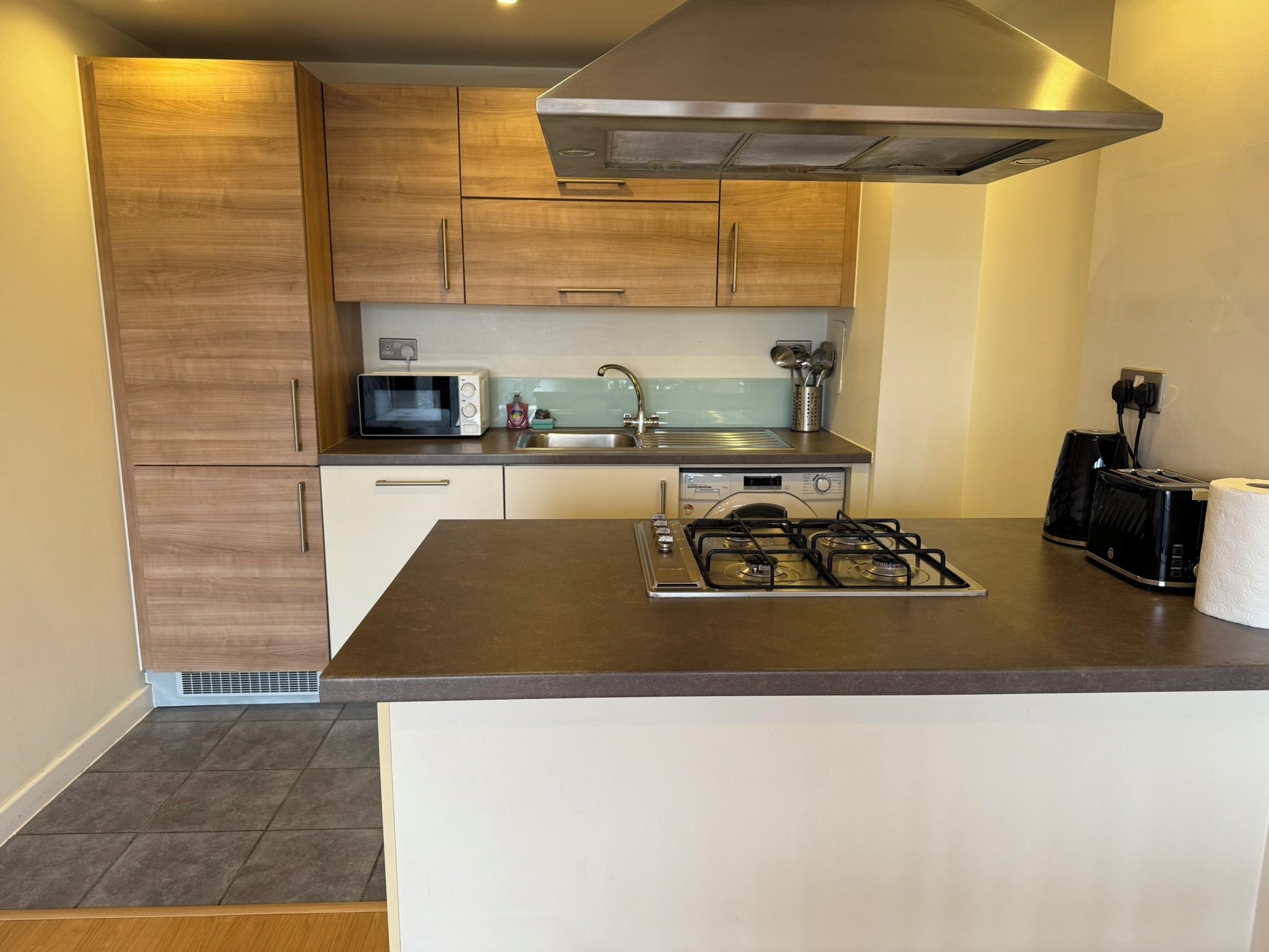 A modern kitchen with wooden cabinets, a microwave, a gas stove, and a toaster.