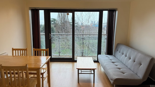 Een kamer met een eettafel, stoelen, een bank en een balkon met een hekwerk.