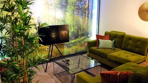 A modern living room with a green sofa, a glass coffee table, and a large flat-screen TV. - "The Church Fields - Dream Stay" Rust nabij natuur & met gratis parkeerplaats (Brunssum)