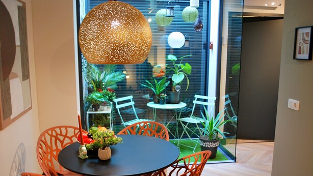 A dining area with a round table and orange chairs, a hanging light fixture, and potted plants. - "The Church Fields - Dream Stay" Rust nabij natuur & met gratis parkeerplaats (Brunssum)