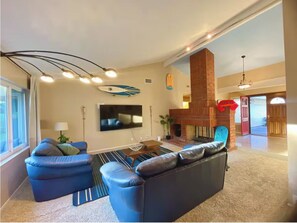 A modern living room with a flat-screen TV, blue leather sofas, a coffee table, and a fireplace. - 15min to Disney - Family Fun Home! (Fullerton)