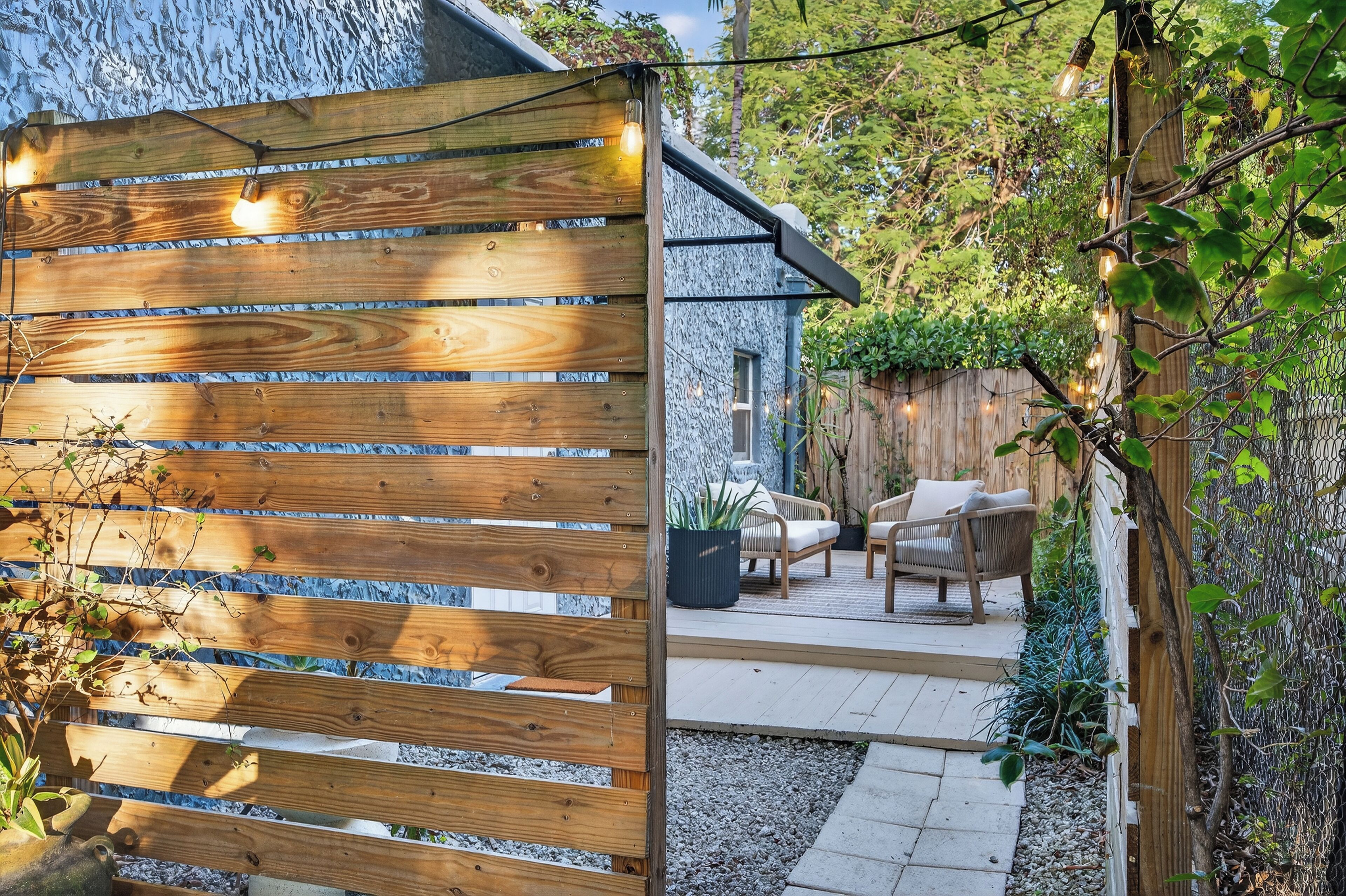 A wooden fence with string lights, a patio with outdoor furniture, and a stone wall.