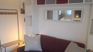 En stue med en rød sofa, to hvide puder, et træsidebord og en indbygget reol.