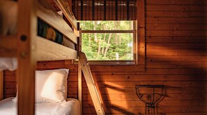 Une chambre rustique en bois, avec un lit superposé, une petite table et une fenêtre donnant sur la forêt.