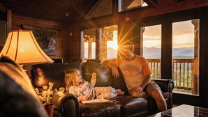 A cozy cabin interior with a leather couch, a lamp, and a view of the outdoors. - Mountain Views, Family Getaway, Pet Friendly, Game Room, Sleeps 9 (Sevierville)