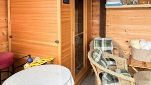 Interior de una cabaña de madera con una mesa redonda, sillas de mimbre, un banco y una cesta de almacenamiento.
