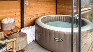 Un jacuzzi en una cabaña de madera con una silla de mimbre y una mesita.