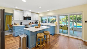 A modern kitchen with white cabinets, a central island with stools, and a view of the outdoor pool area. - Sleeps 12 • Game Room • Theatre • Tiki Bar • Pool (Bradenton)