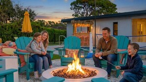 A group of people sitting around a circular fire pit in an outdoor setting with chairs and a thatched-roof structure in the background. - Sleeps 12 • Game Room • Theatre • Tiki Bar • Pool (Bradenton)