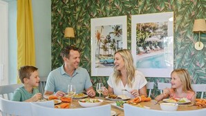 A family dining at a table with tropical wallpaper and framed pictures of a pool and palm trees. - Sleeps 12 • Game Room • Theatre • Tiki Bar • Pool (Bradenton)