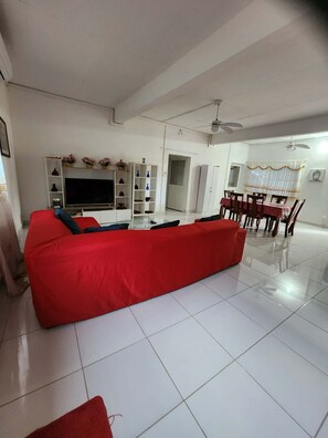Un salón amplio con un sofá rojo, un televisor y una zona de comedor con sillas y una mesa.