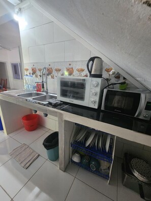 Una cocina compacta con microondas, tostadora, pileta y un escurreplatos pequeño.