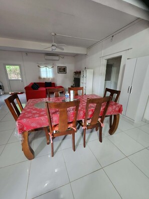 Un comedor con mantel rojo, sillas de madera, un ventilador de techo y un sofá rojo al fondo.