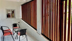 Un petit balcon fermé, doté d’un sol carrelé de carreaux blancs, de deux fauteuils en osier noirs avec des coussins orange, d’une petite table et d’une cloison en lattes de bois.